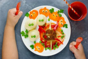 Creative idea for baby dinner or lunch. Funny spider meatball with colorful vegetables garnish shaped ghosts and carrot pumpkins. Concept of healthy meal food for children top view